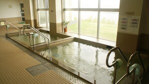 A swimming pool with clear water, metal handrails, and a view of a grassy field through large windows. - Green Stay Nagaura (Suooshima)