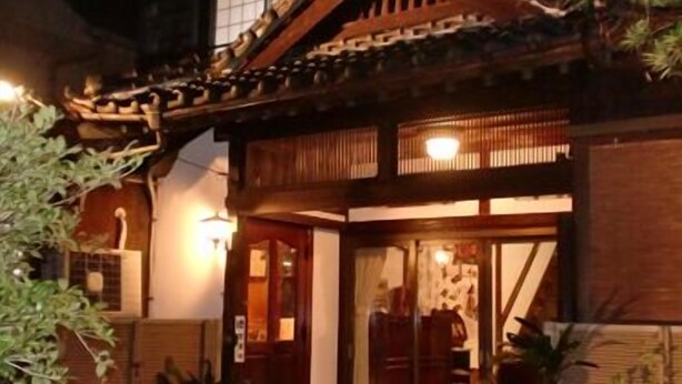 Un edificio de estilo japonés tradicional con fachada de madera, tejado de tejas y una entrada bien iluminada.