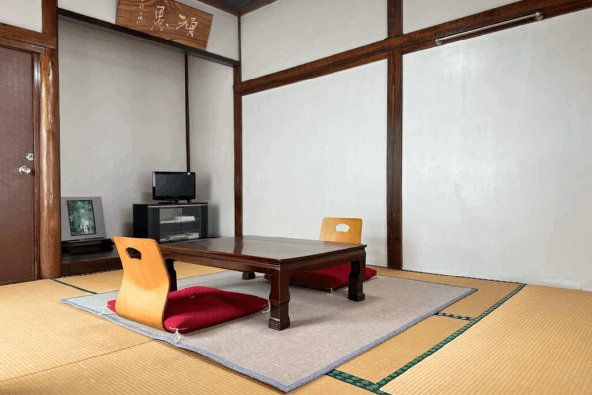 A tatami mat room with a low wooden table, a chair, and a television.