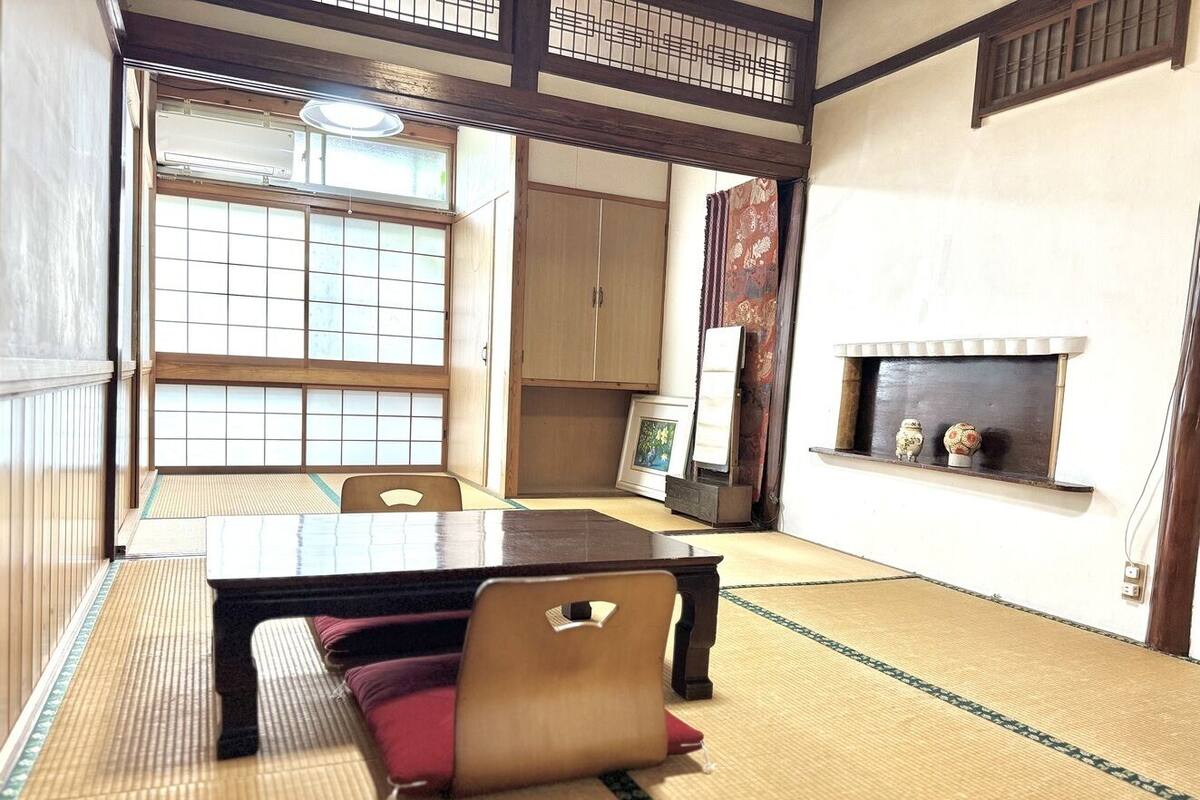 A tatami mat room with a low table and chairs, a traditional Japanese sliding door, and a small shelf with decorative items.