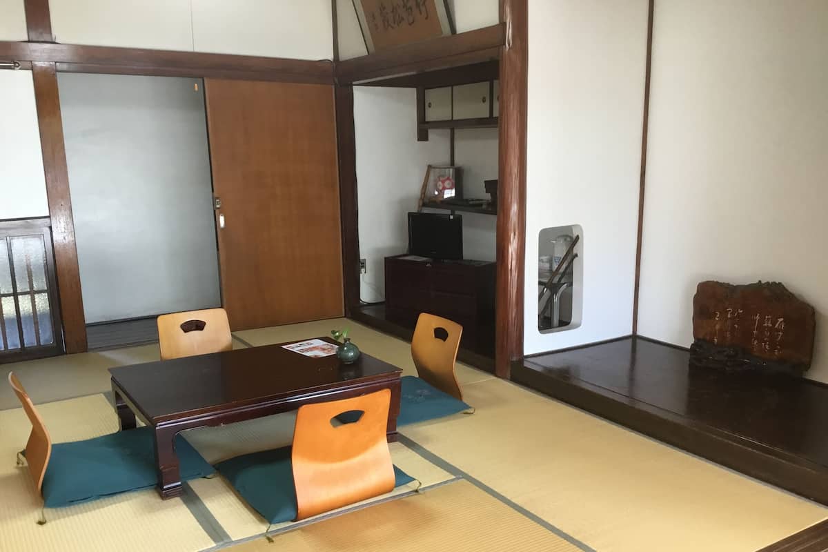 A traditional Japanese-style room with tatami flooring, a low table, and wooden chairs.