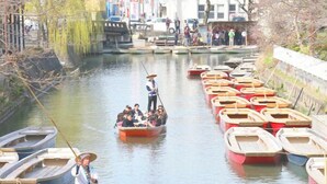 Un río con barcos, una persona en un bote y una multitud en la orilla.