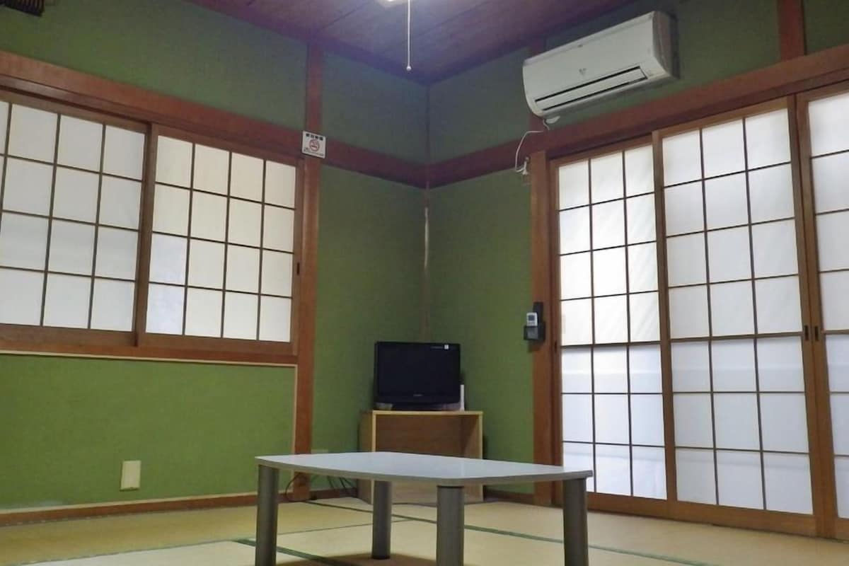 A traditional Japanese room with tatami flooring, sliding shoji doors, and a television on a wooden cabinet.