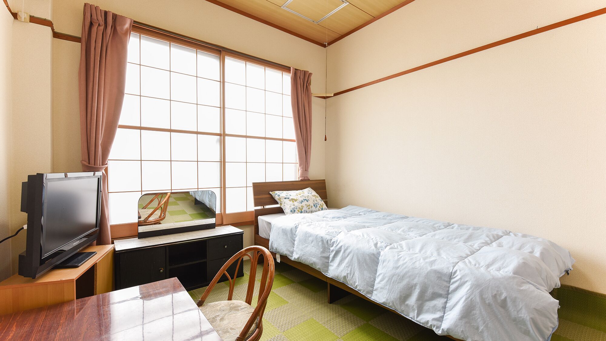 A bedroom with a single bed, a desk with a television, and a chair.