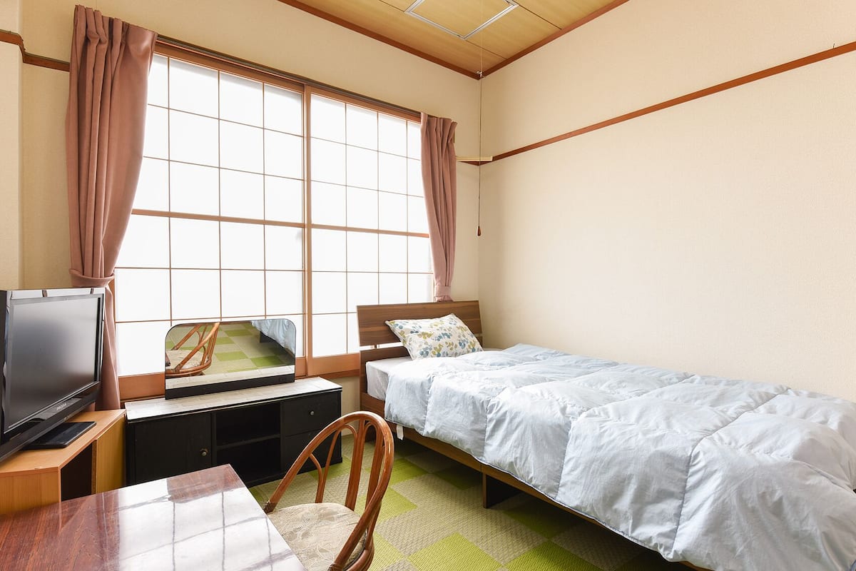 A bedroom with a single bed, a desk with a television, and a chair.