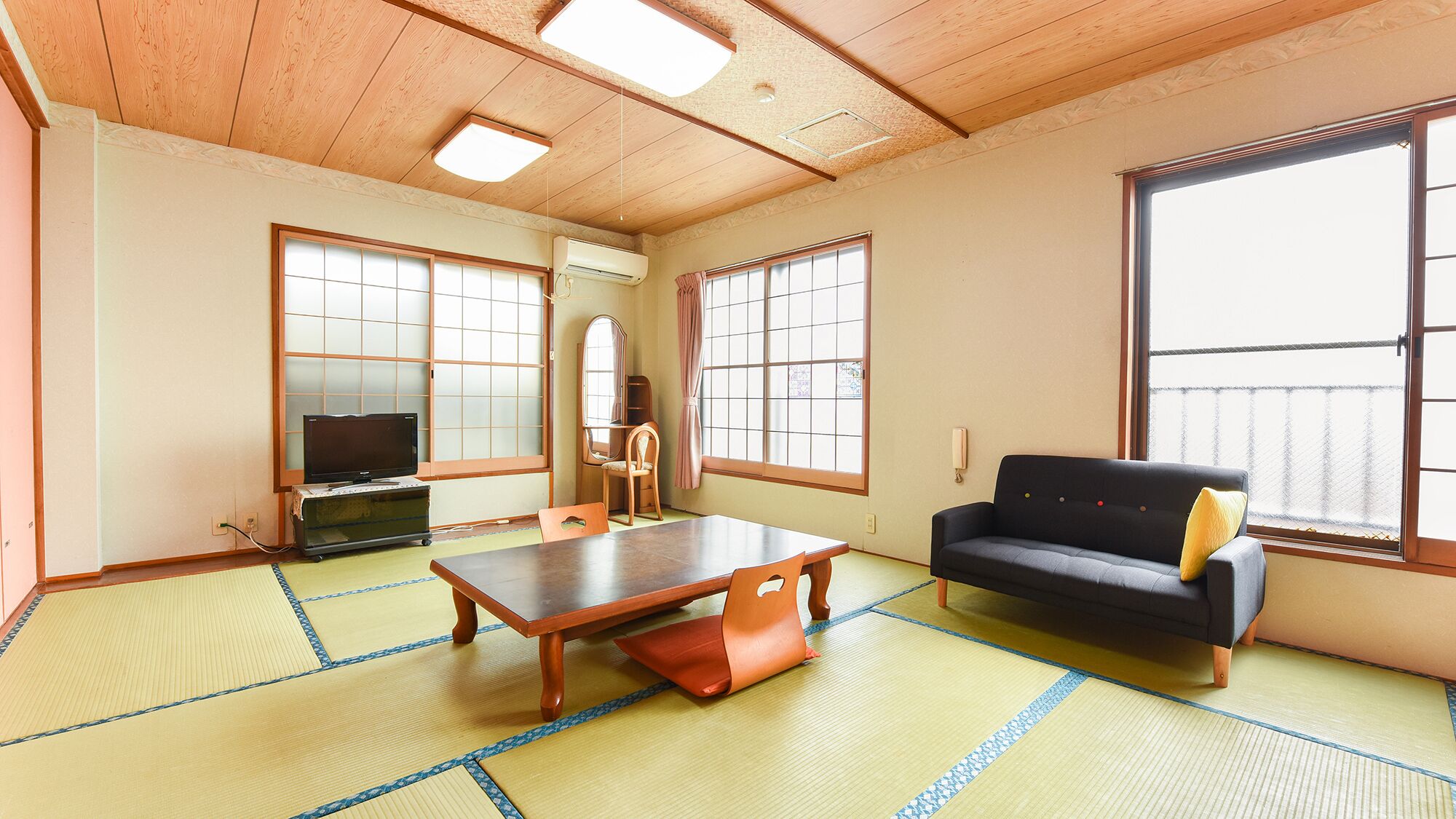 A room with tatami flooring, a sofa, a table, a TV, and large windows.