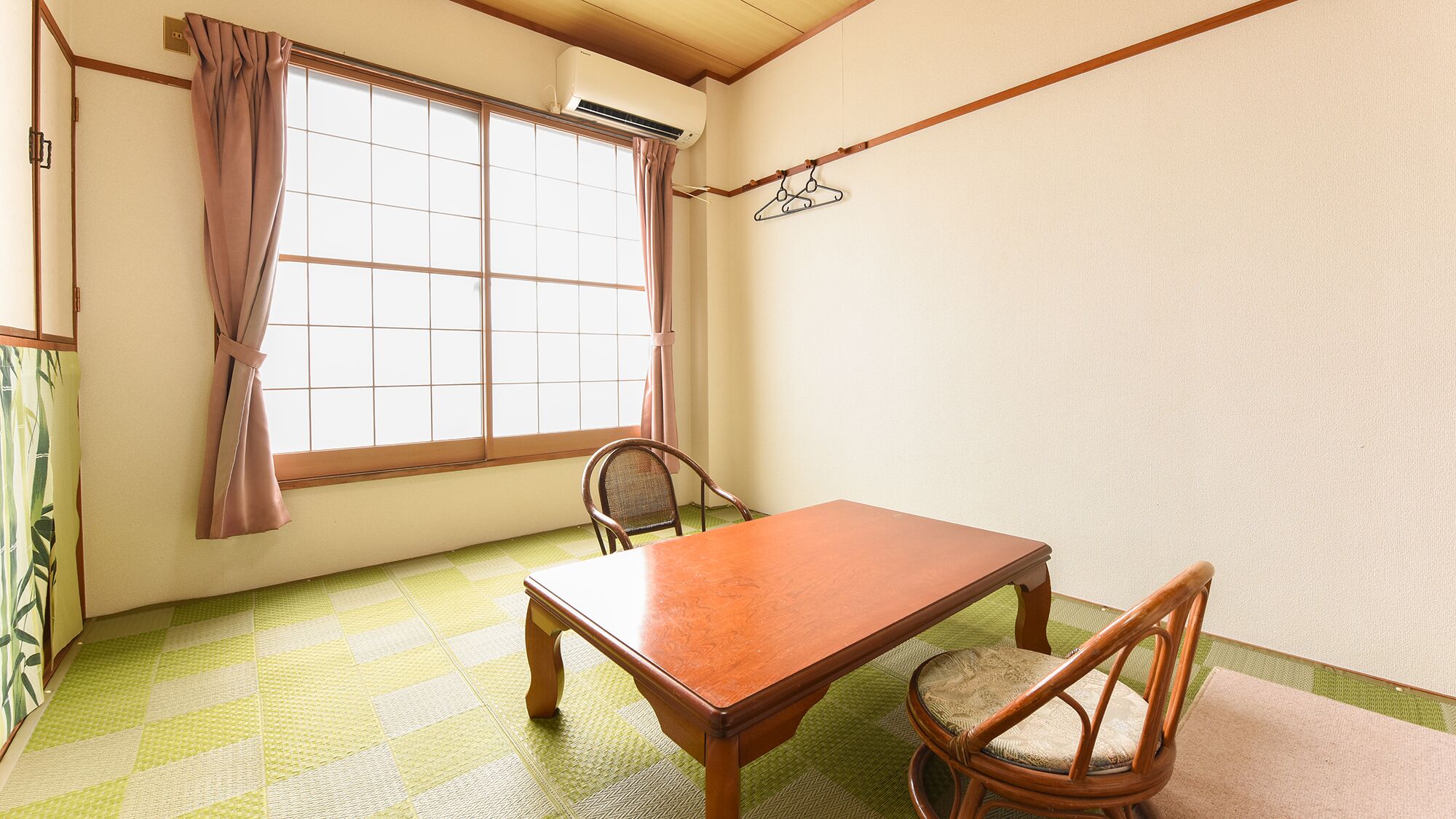 A room with a wooden table, two chairs, a window with curtains, and a hanging light fixture.