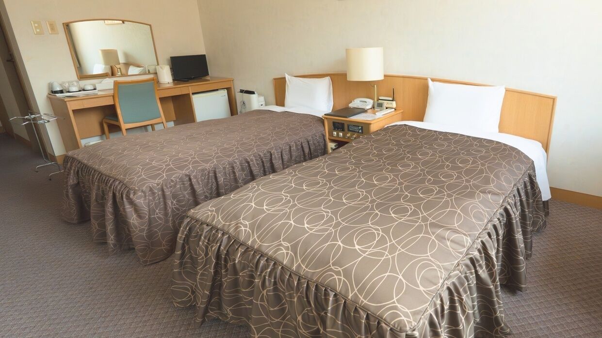 Una habitación de hotel con dos camas, un escritorio, una silla, un espejo, una lámpara y un teléfono.