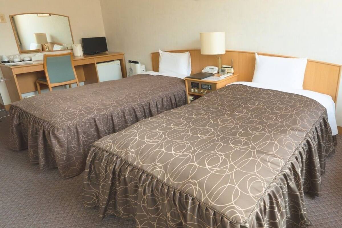 Una habitación de hotel con dos camas, un escritorio, una silla, un espejo, una lámpara y un teléfono.