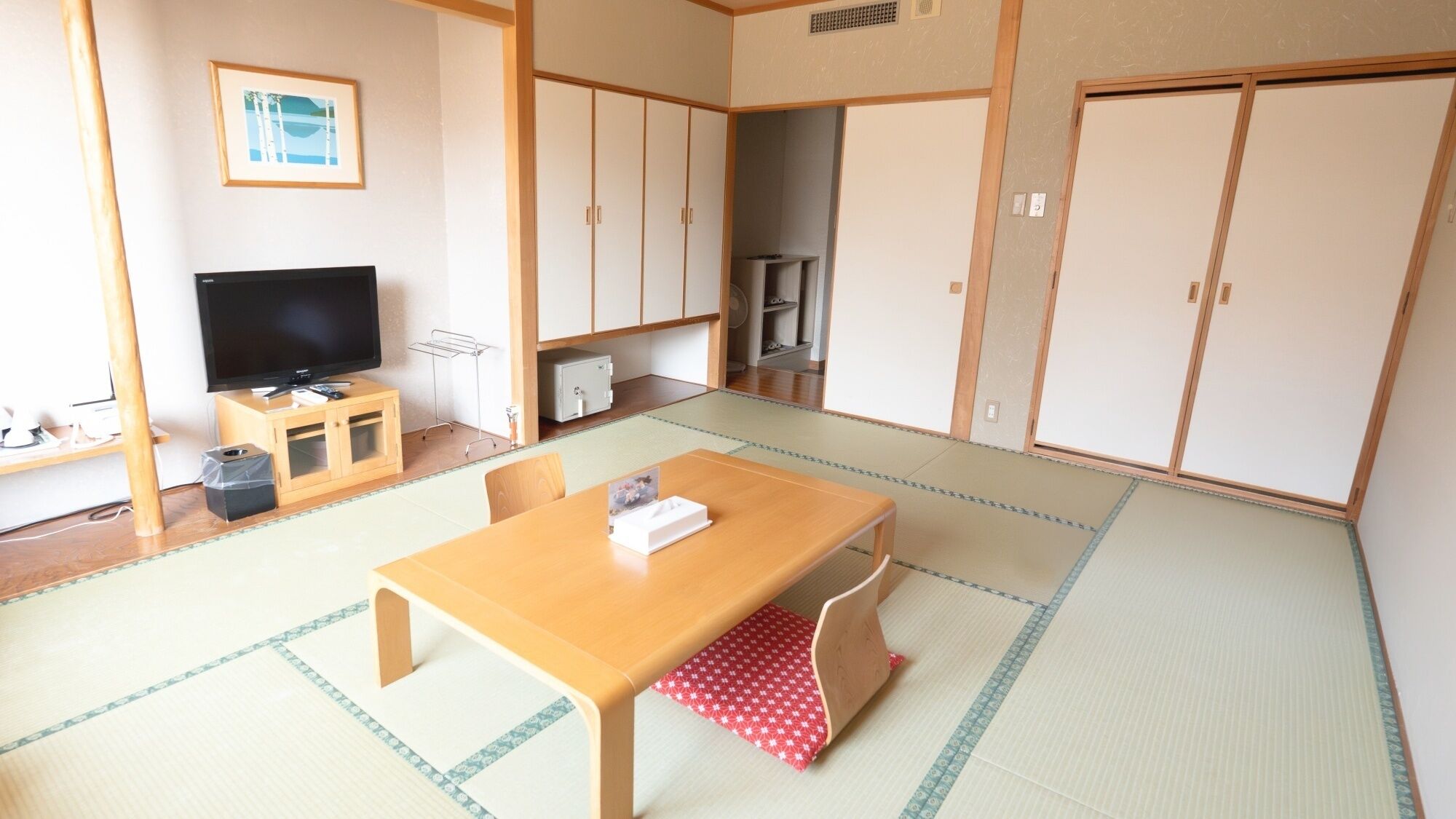 Una habitación japonesa tradicional con suelo de tatami, televisión, un armario y una mesa con posavasos.