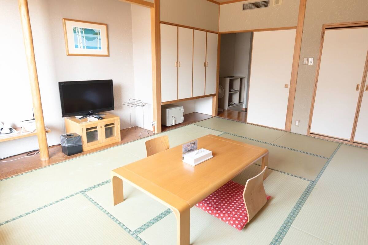 Una habitación japonesa tradicional con suelo de tatami, televisión, un armario y una mesa con posavasos.