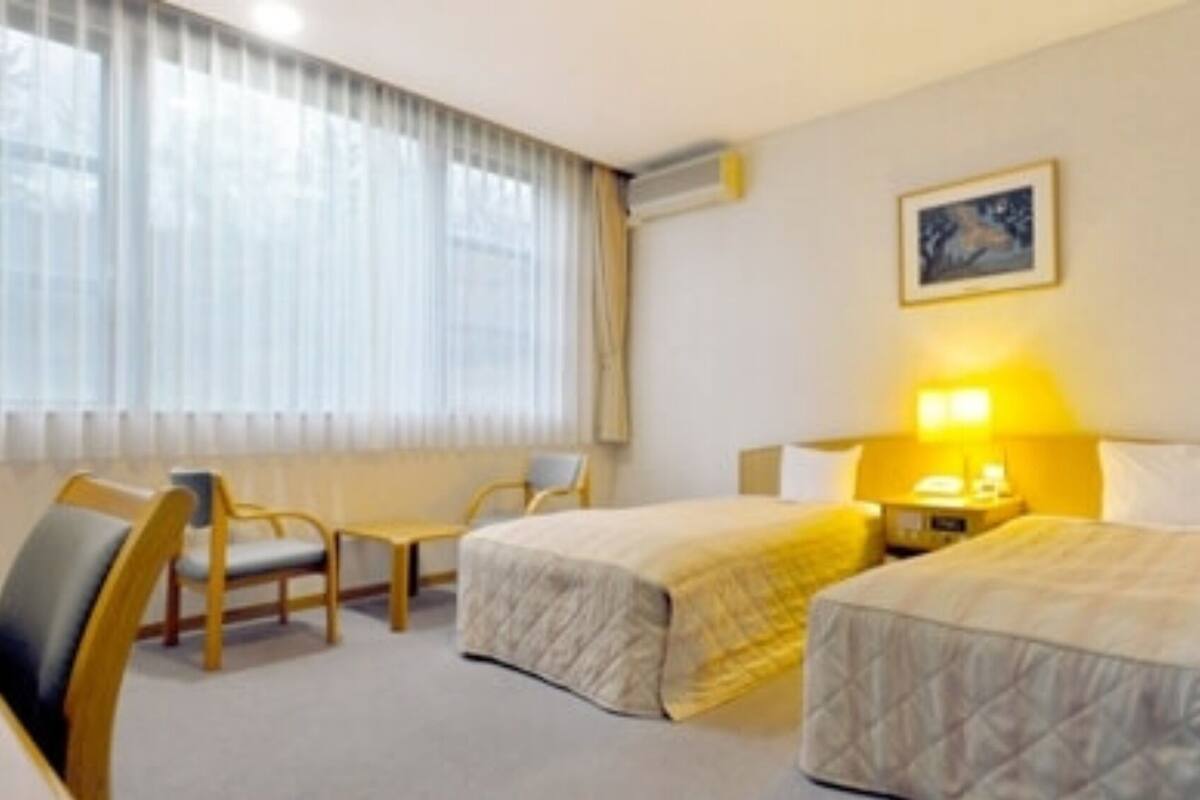 Habitación de hotel con dos camas, un escritorio, una silla y un ventanal con cortinas.