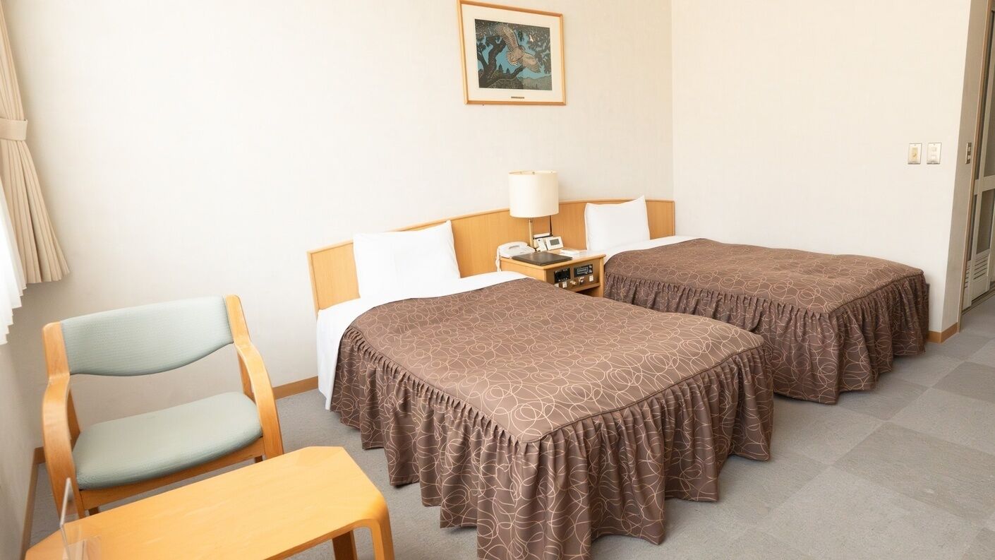 Habitación de hotel con dos camas, una silla, una mesa, una lámpara y un cuadro en la pared.