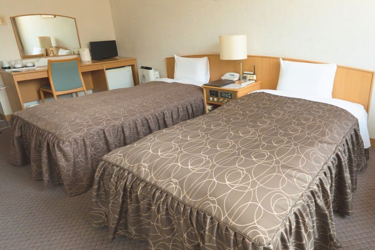 Una habitación de hotel con dos camas, un escritorio, una silla, un espejo, una lámpara y un teléfono.