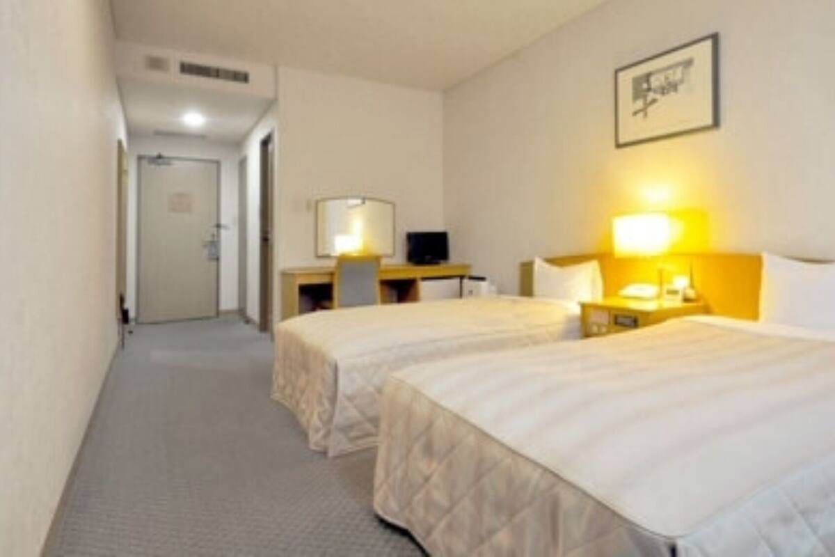 Habitación de hotel con dos camas, un escritorio, una silla y un televisor.