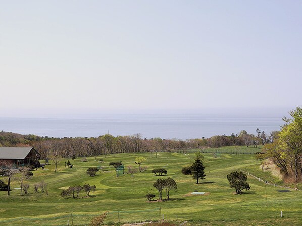 A rural landscape with a house, open fields, and a distant view of the ocean.