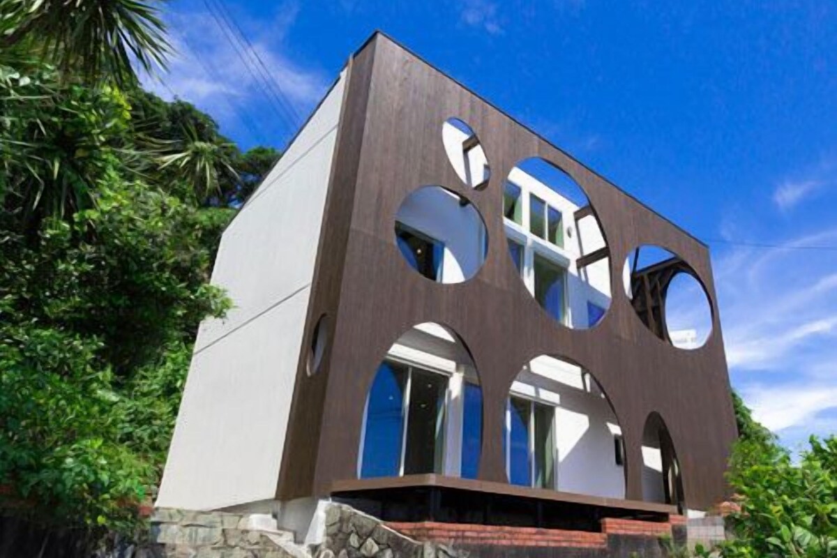 A modern two-story building with circular cutouts on the facade, surrounded by greenery.