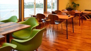 A modern dining area with wooden tables and chairs, large windows offering a view of the sea, and an air conditioning unit on the wall. - Epurontei (Miyazaki)