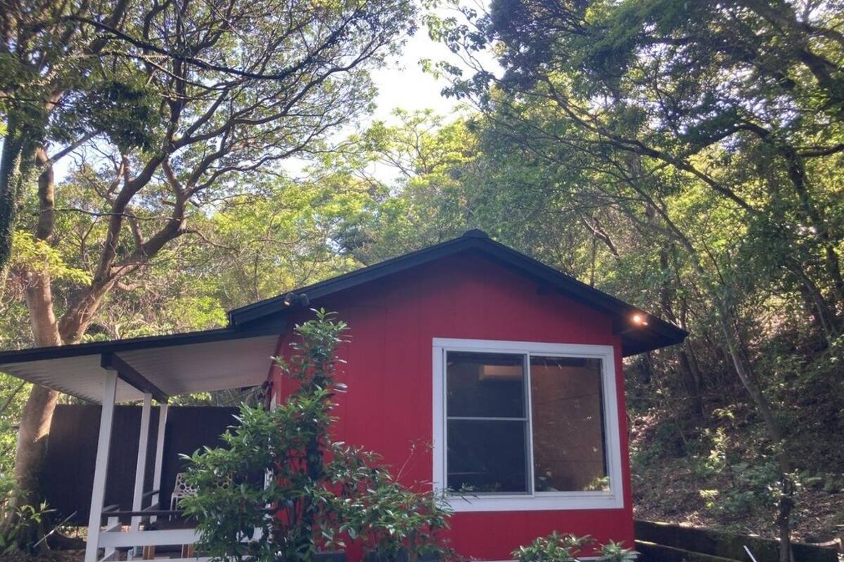 A red cabin with a white window and a porch, surrounded by trees.