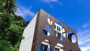Ein modernes, zweistöckiges Gebäude mit kreisförmigen Aussparungen an der Fassade, umgeben von Grünflächen.