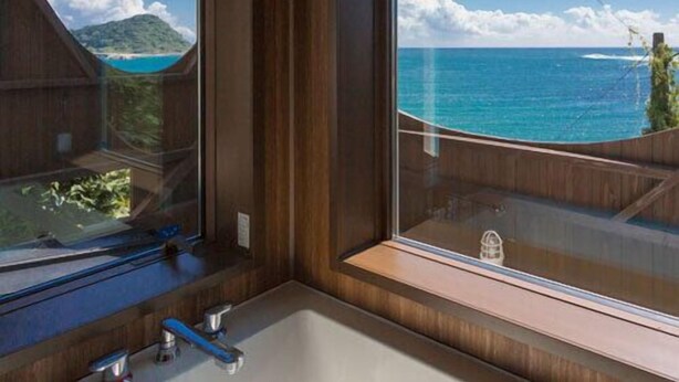 Ein Badezimmer mit einem großen Fenster, das Blick auf den Ozean und ein Gebirge bietet.