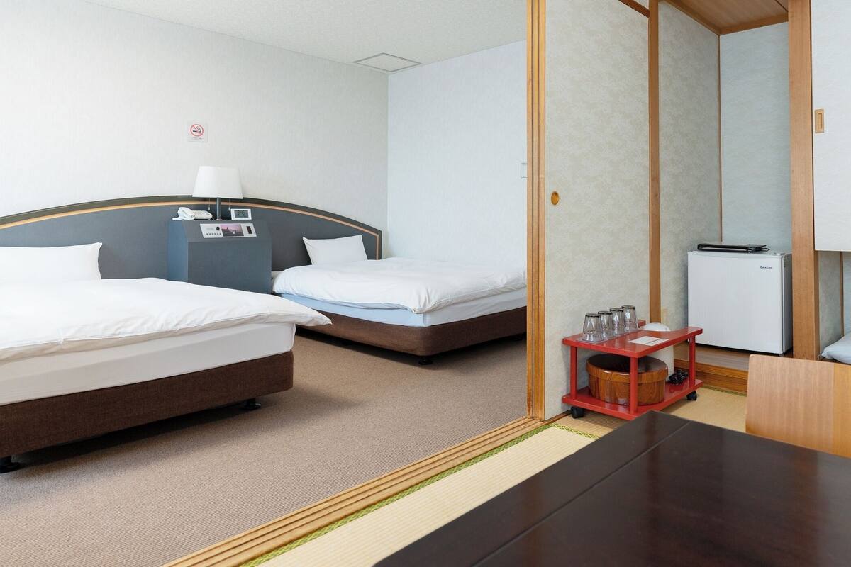 Une chambre d’hôtel avec deux lits, un bureau, un minibar et une petite table avec des verres.