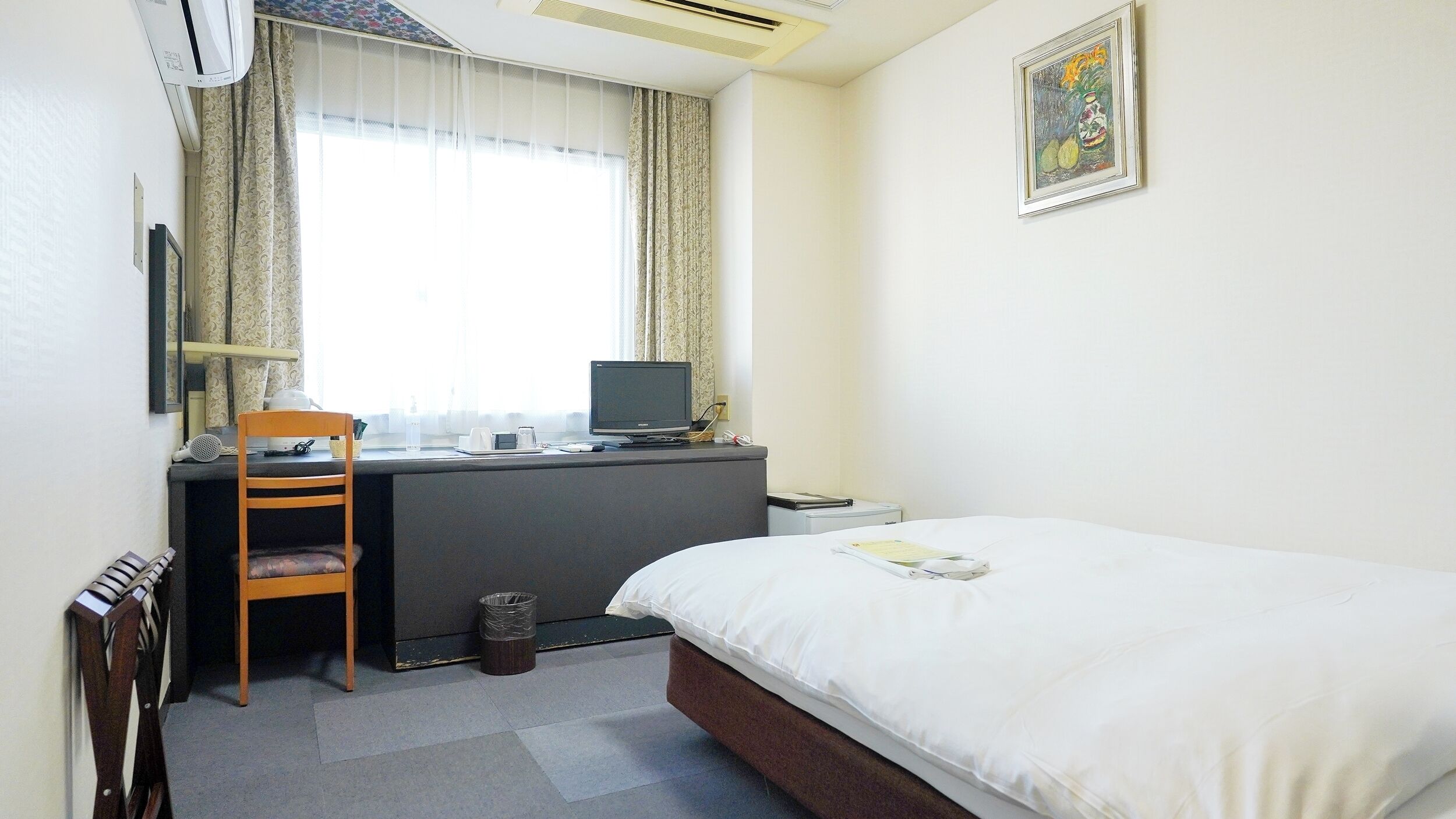 A hotel room with a bed, desk, chair, and a window with curtains.