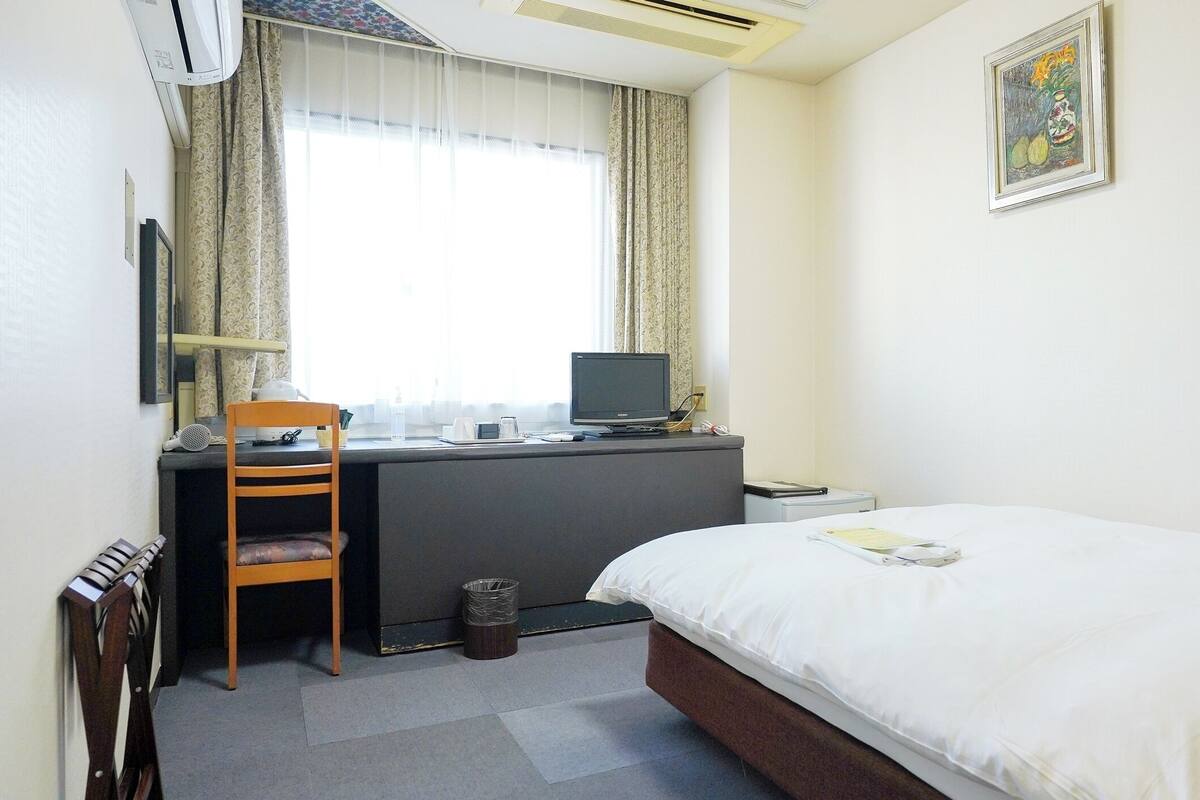 Une chambre d’hôtel avec un lit, un bureau, une chaise et une fenêtre avec des rideaux.
