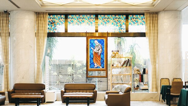 A spacious lobby with a large stained glass window, a seating area with sofas, and a bookshelf with books and decorative items. - Hotel Saint Hill Nagasaki (Nagasaki)