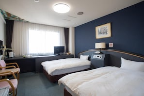 A hotel room with two beds, a desk with a computer, a chair, and a window with curtains.