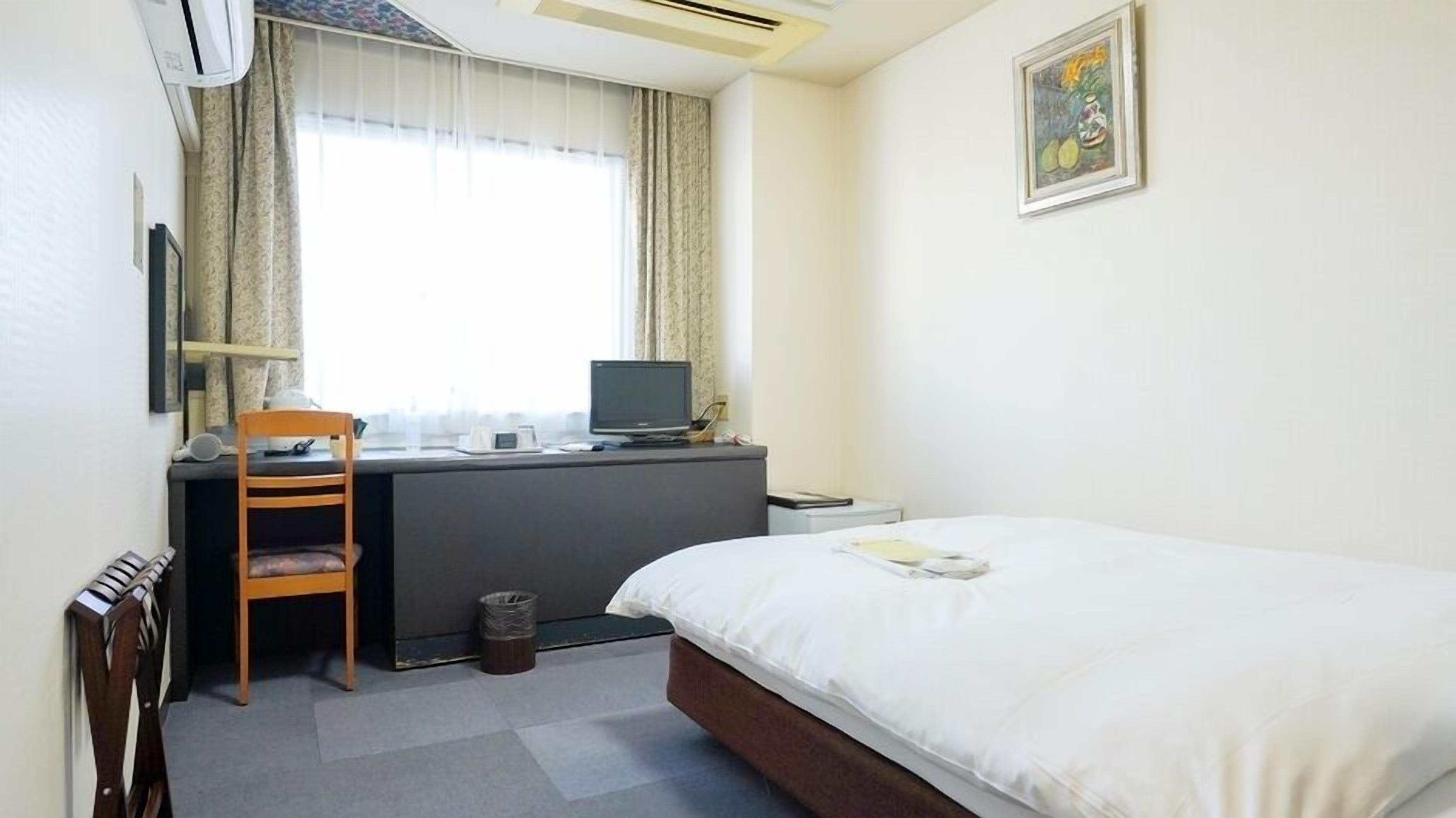 A hotel room with a bed, desk, chair, and a window with curtains.