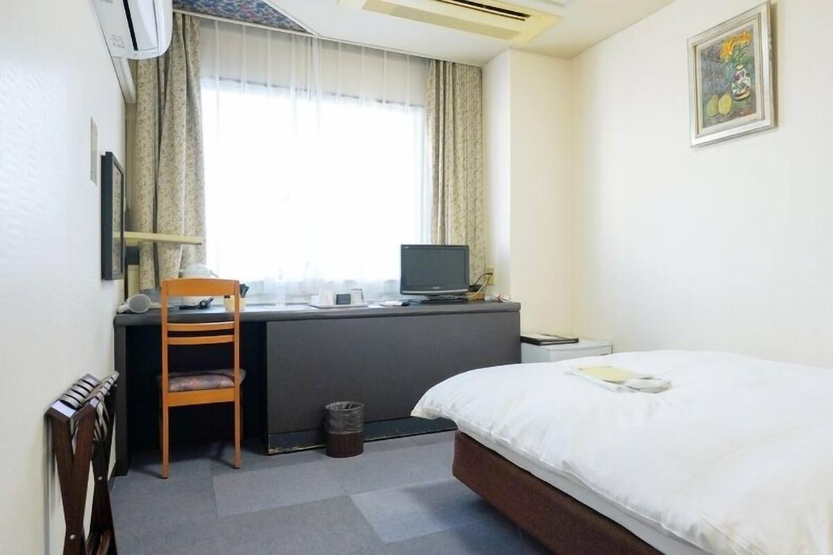 Une chambre d’hôtel avec un lit, un bureau, une chaise et une fenêtre avec des rideaux.