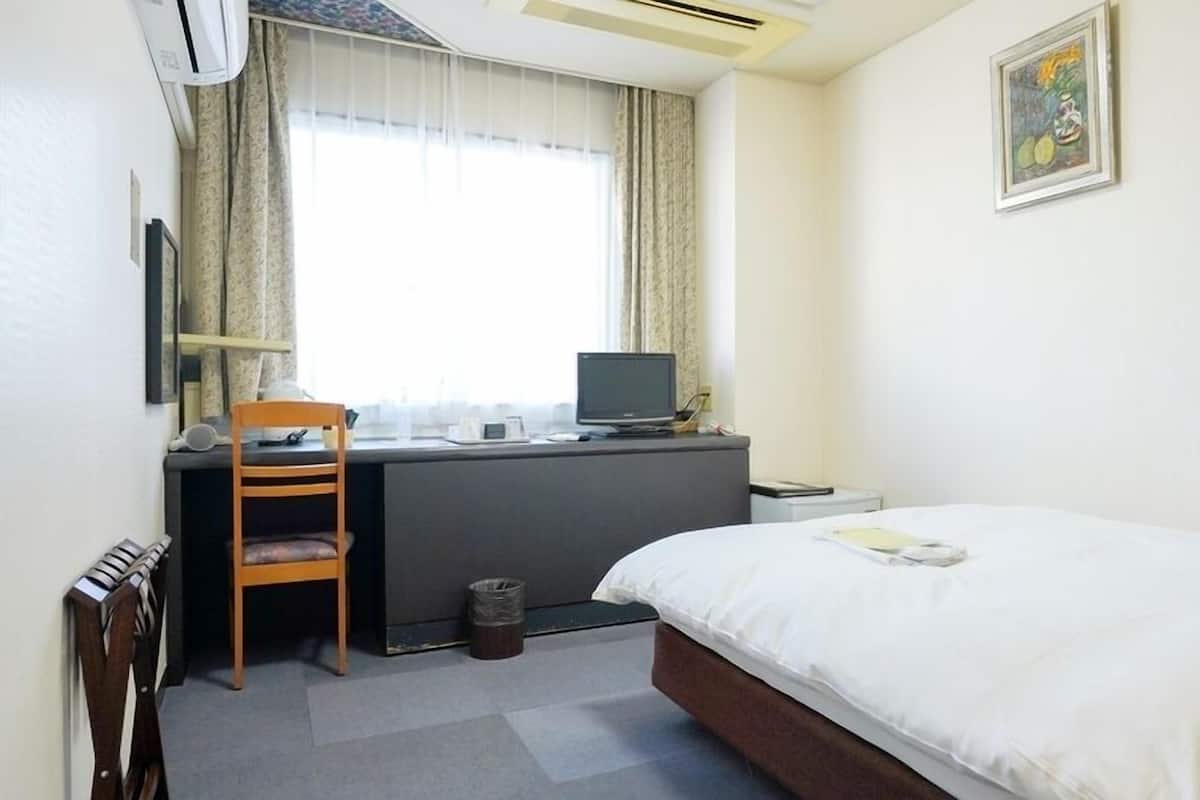 Una habitación de hotel con cama, escritorio, silla y ventana con cortinas.
