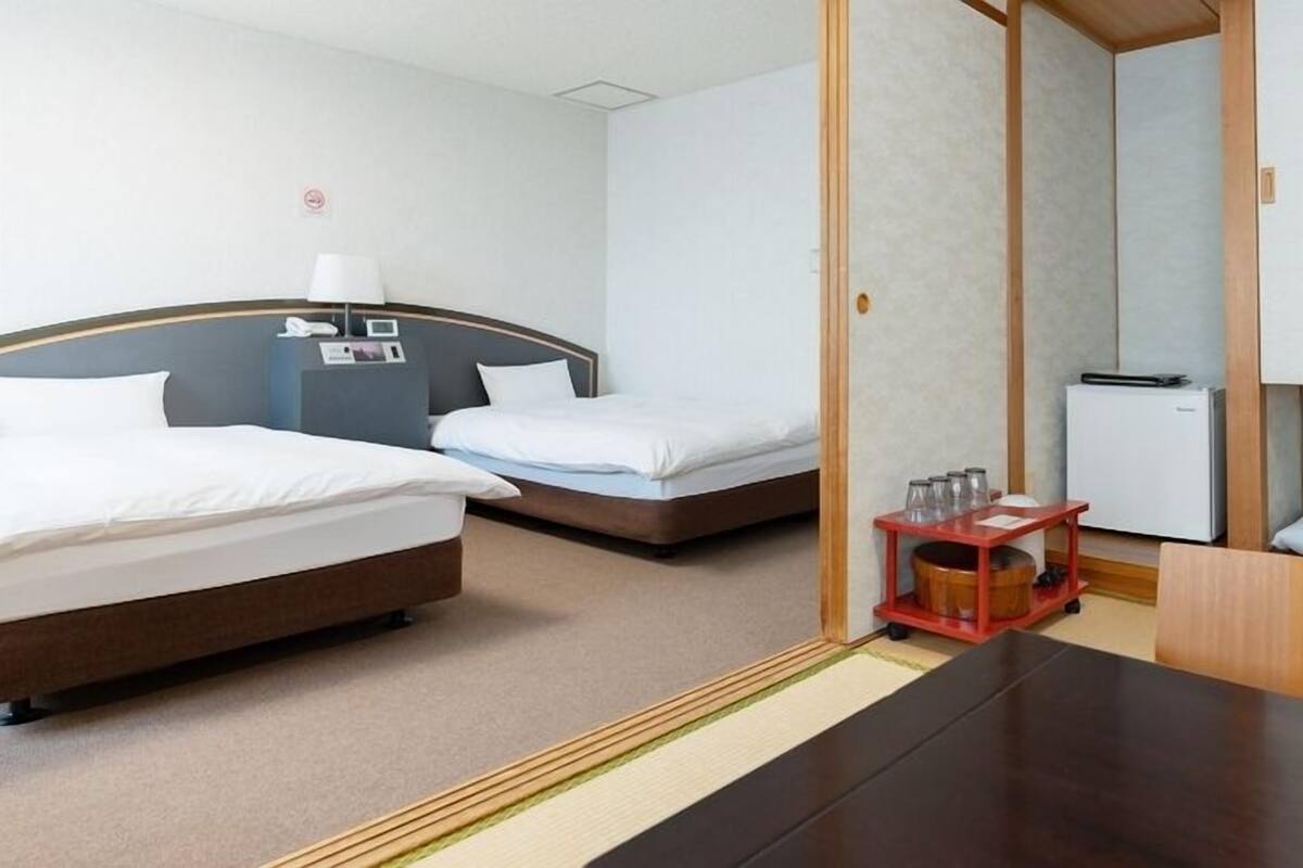 Une chambre d’hôtel avec deux lits, une petite table avec des verres, un réfrigérateur et une armoire en bois.