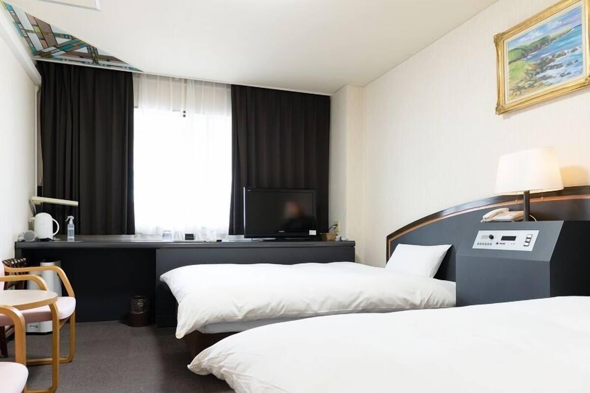 Une chambre d’hôtel avec deux lits, un bureau avec une télévision, une chaise et un tableau au mur.