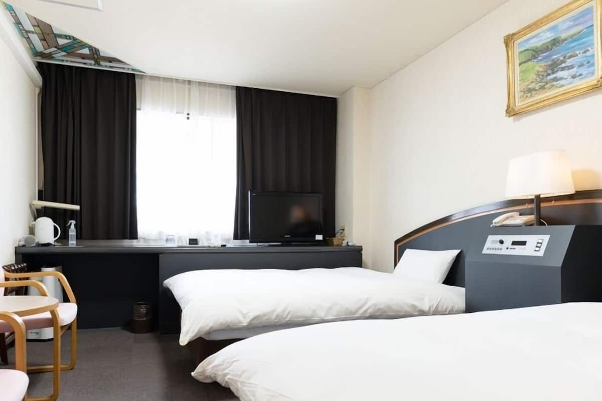 Habitación de hotel con dos camas, un escritorio con televisor, una silla y un cuadro en la pared.