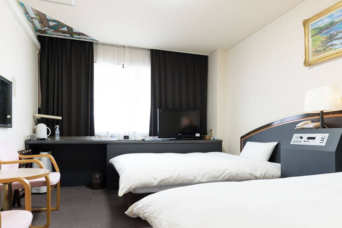 Une chambre d’hôtel avec un lit, un bureau avec une télévision, une chaise et une petite table.