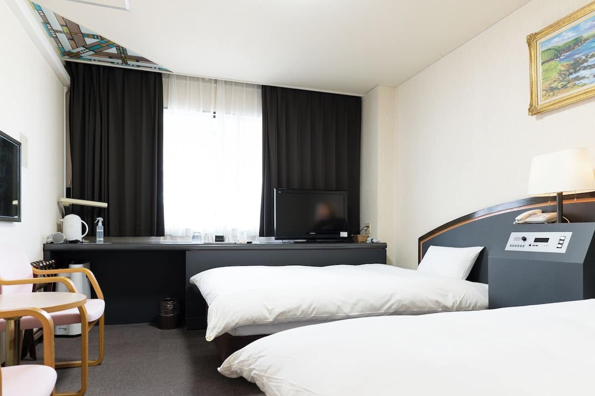 Una habitación de hotel con una cama, un escritorio con televisor, una silla y una mesita.