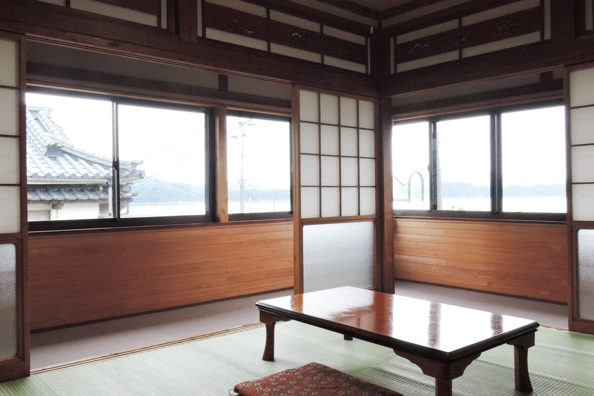 A traditional Japanese room with tatami flooring, sliding shoji doors, and a view of a traditional building.