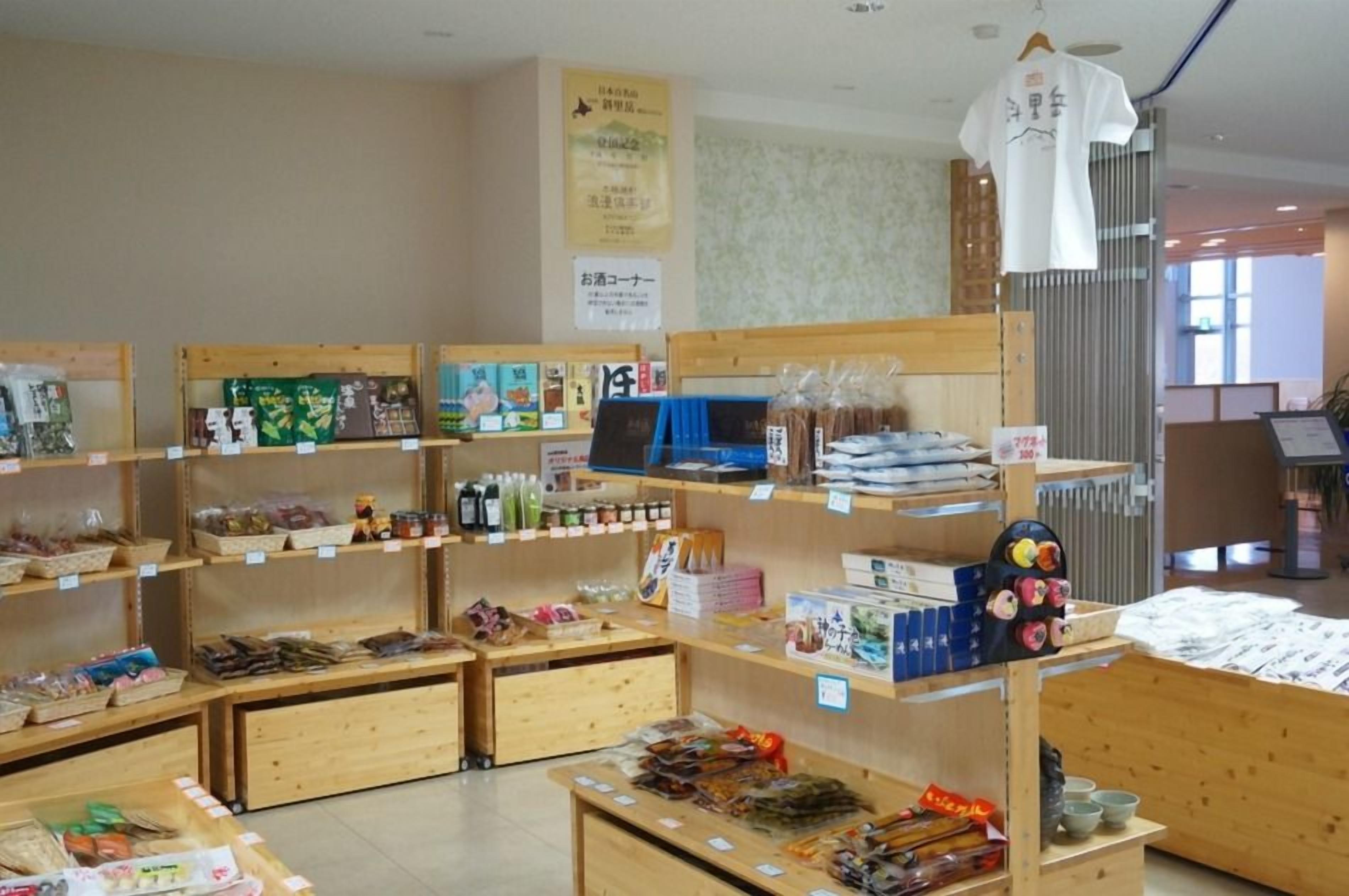 Una tienda con estantes de madera llenos de diversos productos envasados, un mostrador de exhibición con artículos y una camisa blanca colgada.
