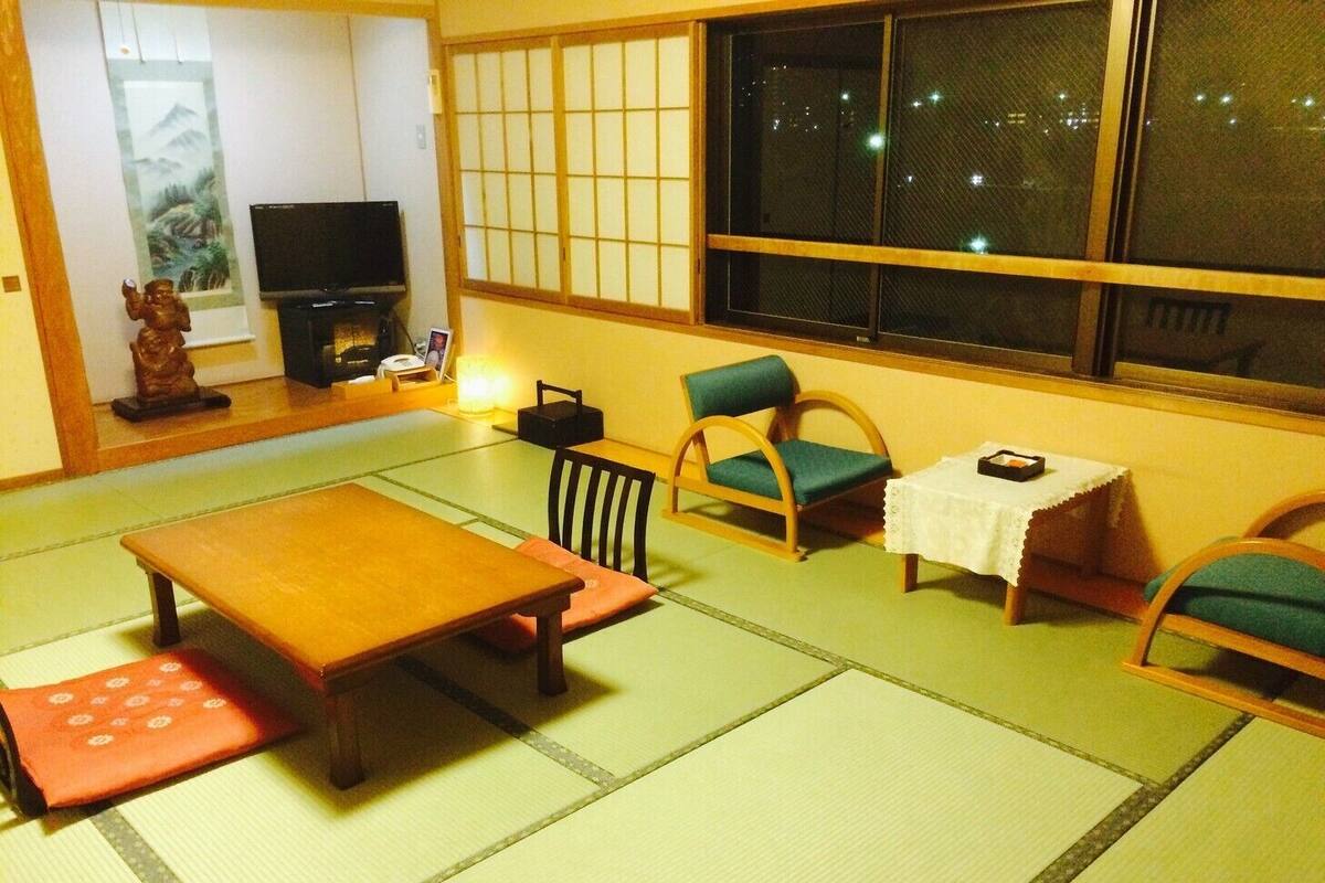 A tatami mat room with a low table, chairs, a television, and a decorative statue.