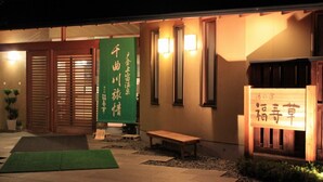 A traditional Japanese building with sliding doors, a green banner with Japanese characters, a wooden bench, and a signboard with Japanese characters. - Tokurakamiyamada Onsen Yu No Yado Fukujuso (Chikuma)