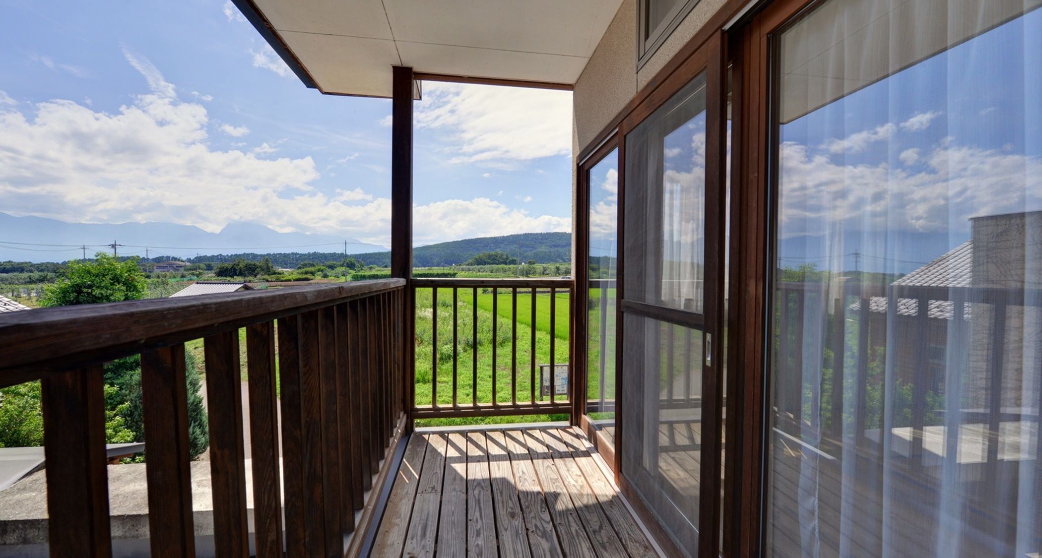 Un balcón de madera con vistas a un paisaje verde y montañas lejanas.
