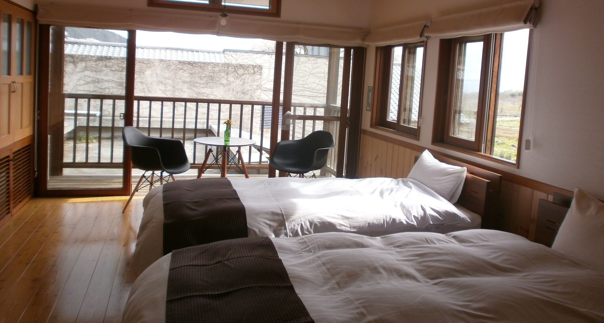 Une chambre avec deux lits, une petite table, deux chaises et de grandes fenêtres.