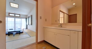 A traditional Japanese room with tatami flooring, a tatami mat table, a wooden cabinet with a mirror, and a sliding door leading to another room. - Oishii Gakko (Hokuto)