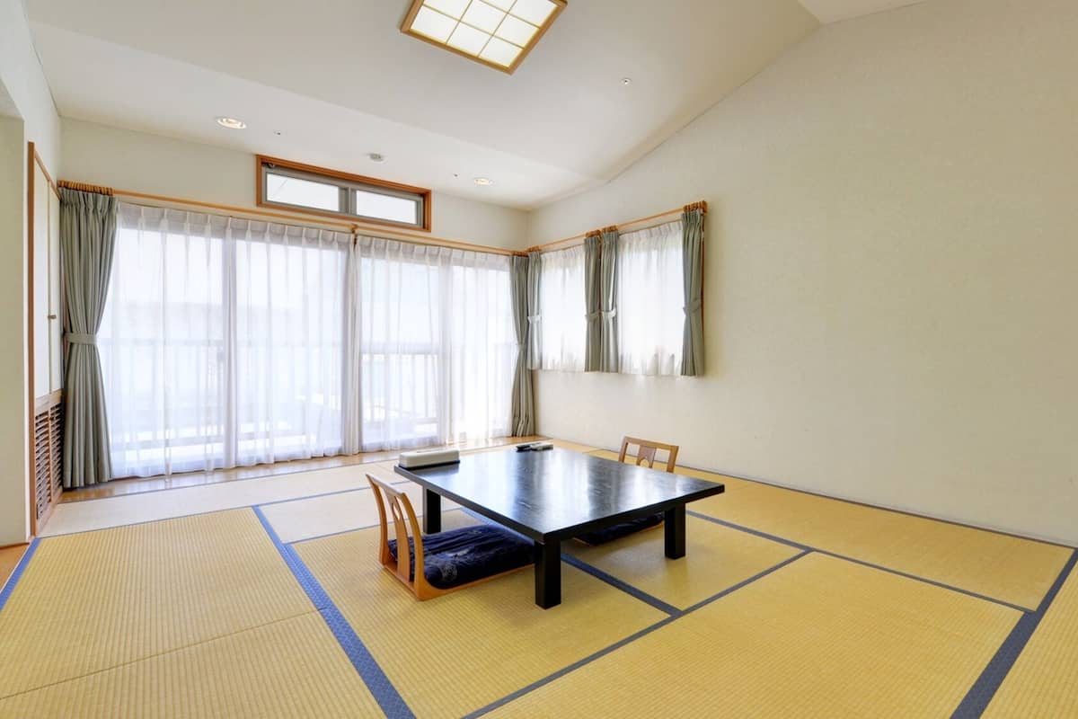 A room with tatami mats, a low table, a chair, and large windows with curtains.