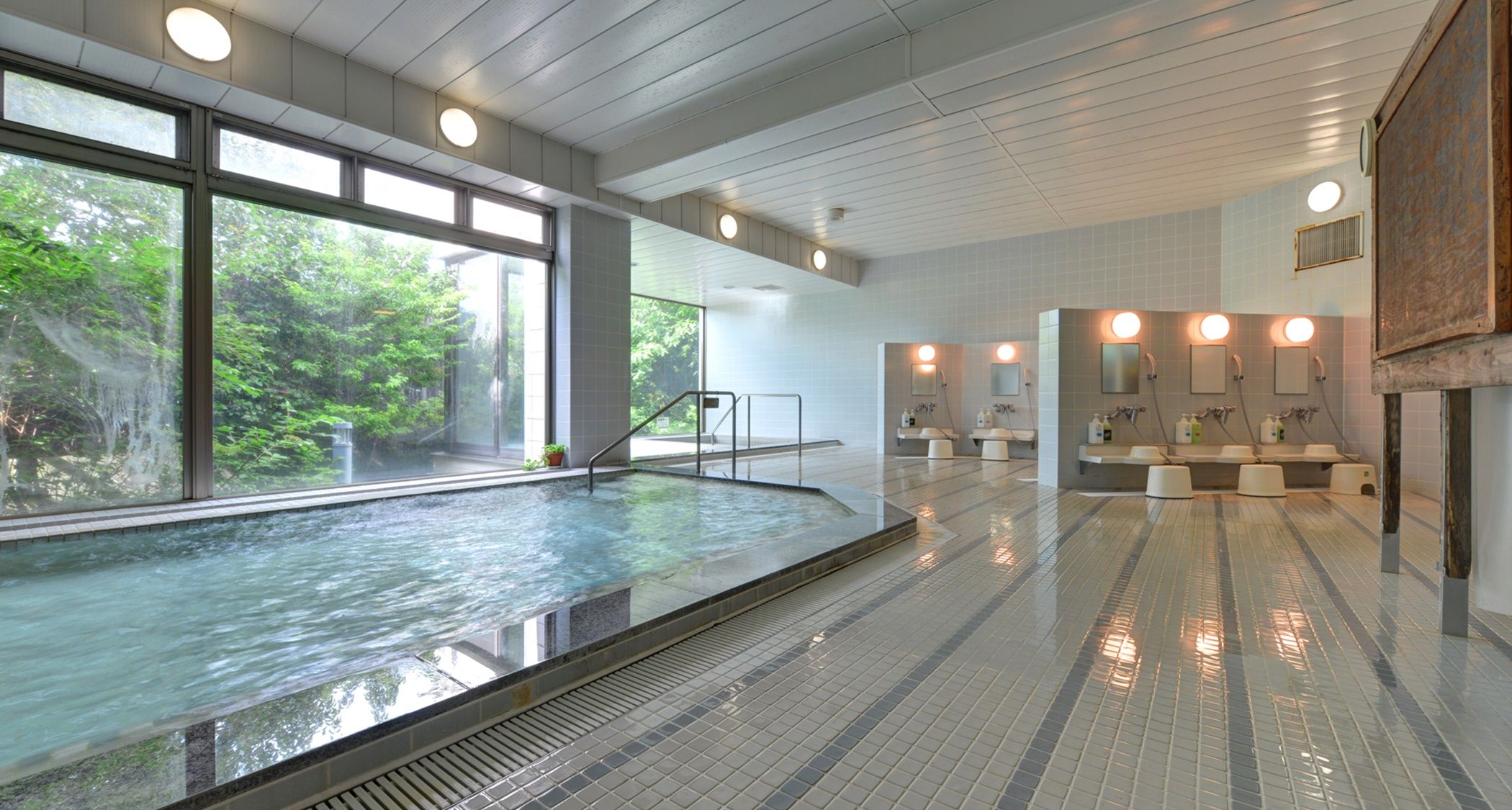 Een modern binnenzwembad met glazen wanden, een betegelde vloer en een goed verlichte badkamer met wastafels en spiegels.