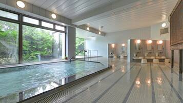 Een modern binnenzwembad met glazen wanden, een betegelde vloer en een goed verlichte badkamer met wastafels en spiegels.