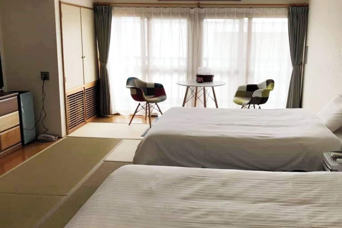 A hotel room with two beds, a desk, a chair, and a television.