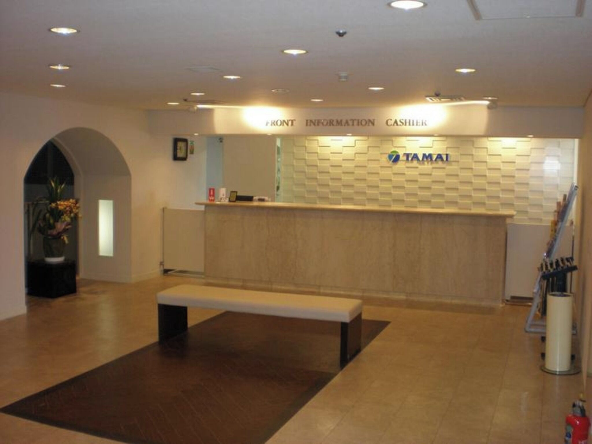 Een receptie met een bank, een balie met de tekst 'FRONT INFORMATION CASHIER' en een muur met het 'TAMAI'-logo.